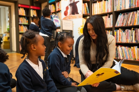 2 children reading book with adult in library